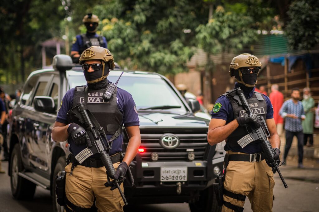 SWAT team members in tactical gear standing by a police vehicle during an operation. Outdoors urban setting.