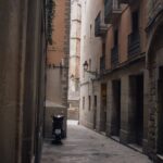 A quiet, narrow alley in Barcelona featuring a parked motor scooter and historic buildings.