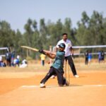Cricket player skillfully hitting a ball during a lively outdoor match on a sunny day.