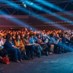 Vibrant image of a diverse audience seated in a large auditorium, highlighted by dynamic stage lighting.