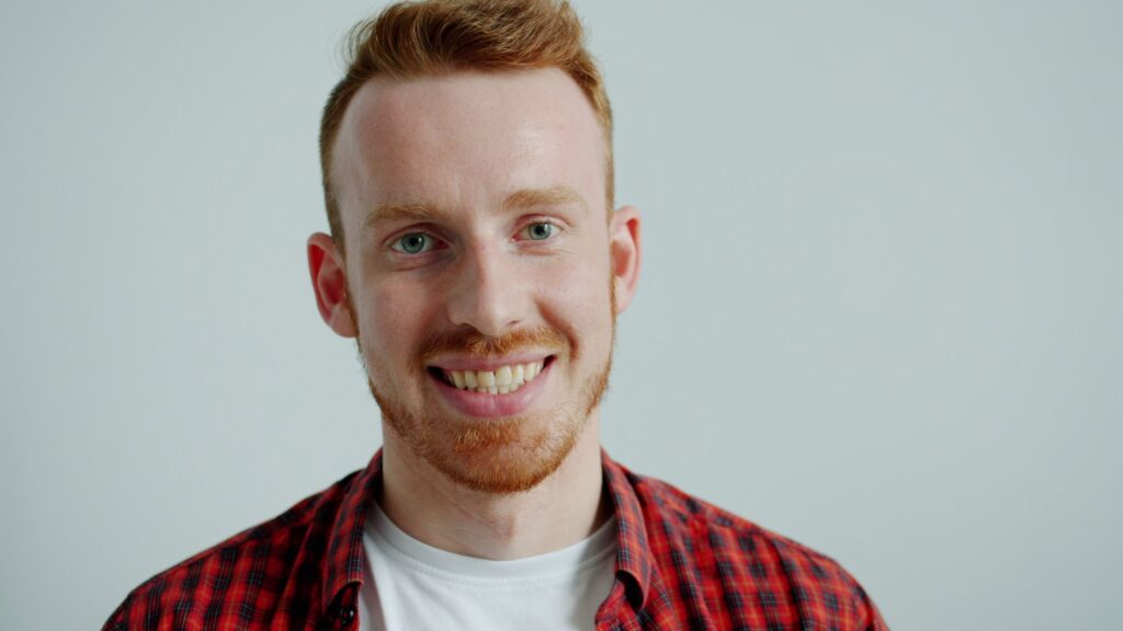 Portrait of a smiling man in a red plaid shirt against a plain background.