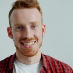 Portrait of a smiling man in a red plaid shirt against a plain background.