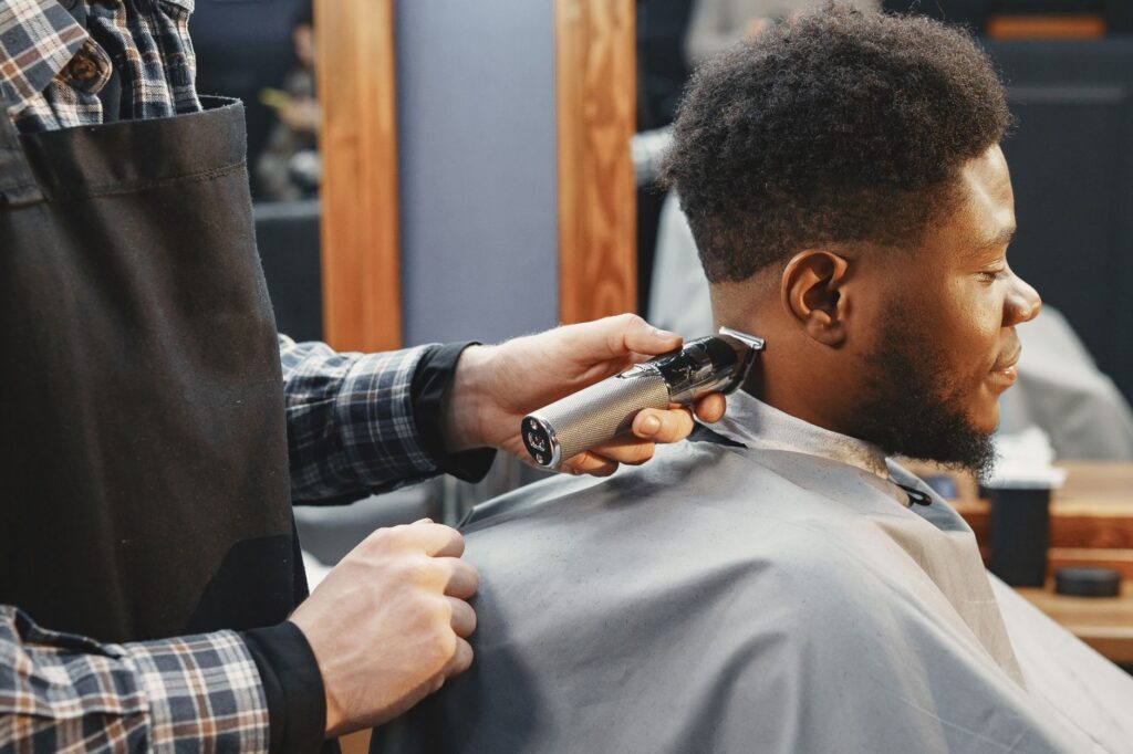 A barber trims an adult man's hair using clippers in a contemporary salon setting.