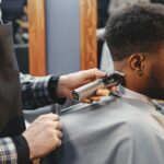 A barber trims an adult man's hair using clippers in a contemporary salon setting.