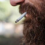 A detailed close-up of a bearded man smoking a cigarette outdoors, showcasing lifestyle choices.