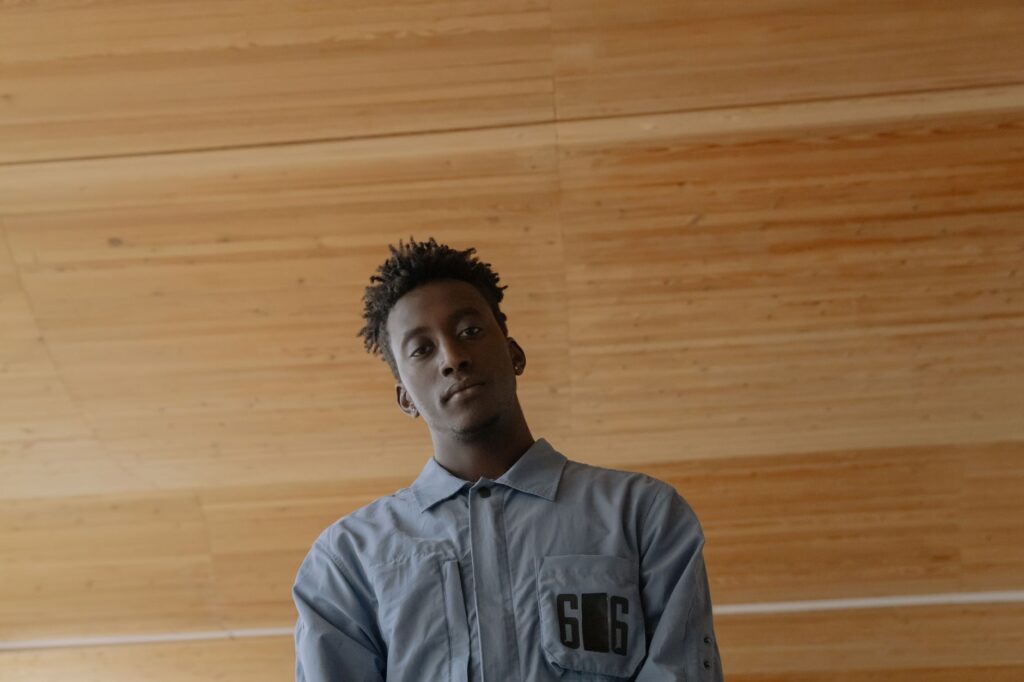 Low-angle shot of a young man in a blue shirt against a wooden ceiling background.