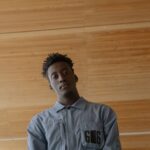 Low-angle shot of a young man in a blue shirt against a wooden ceiling background.