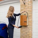 A woman using a home electric vehicle charger on a brick wall in a garage.