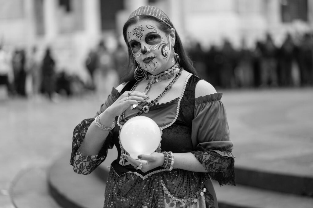A woman in Catrina makeup holds a crystal ball during a cultural event.