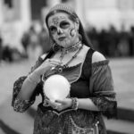 A woman in Catrina makeup holds a crystal ball during a cultural event.