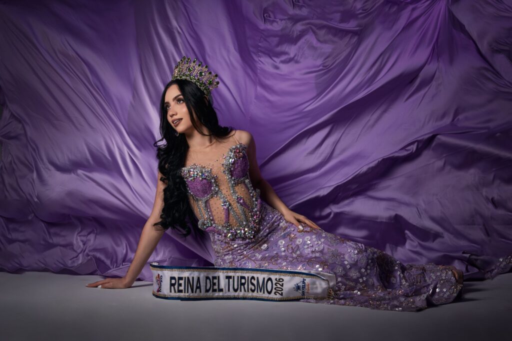 Pageant winner in ornate purple gown with crown, posing elegantly.
