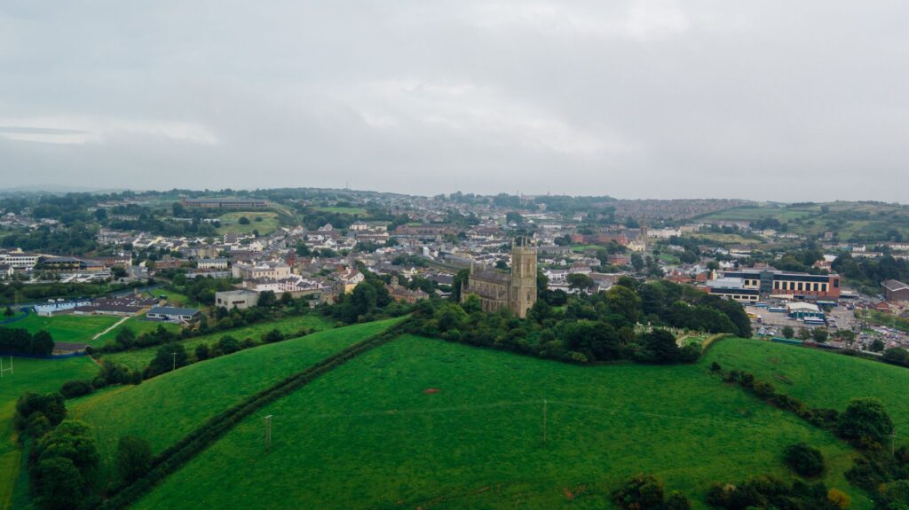 Aerial view capturing a vast green landscape with a charming town and historic architecture under a cloudy sky.