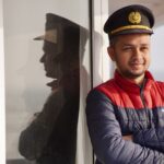 A ship officer in uniform reflects on glass, displaying confidence against a serene sea backdrop.