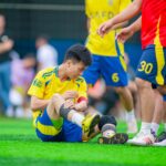 Amateur soccer player sitting on grass, nursing a leg injury during game in Hanoi, Vietnam.