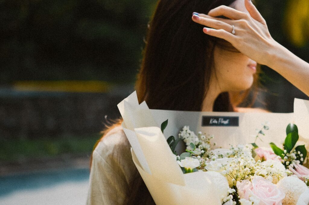 A woman with long hair holds a bouquet of soft-colored flowers outdoors, creating an elegant and serene atmosphere.