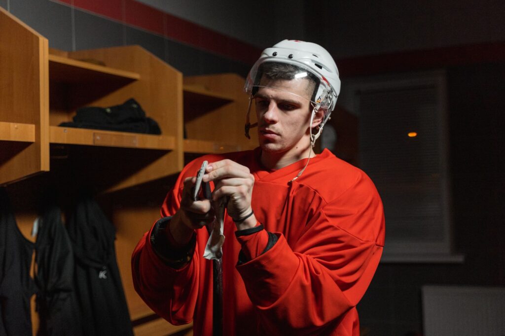 Male hockey player in locker room preparing stick, deep in focus.