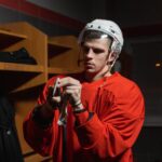 Male hockey player in locker room preparing stick, deep in focus.