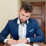 Confident businessman in a suit signing a contract at the office desk.