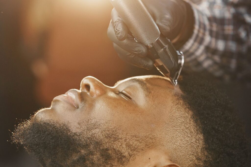 Barber using clippers to trim a client's hair in a bright, relaxed setting.