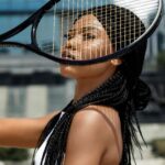 Fashionable young woman with braided hair posing with a tennis racket in an urban setting.