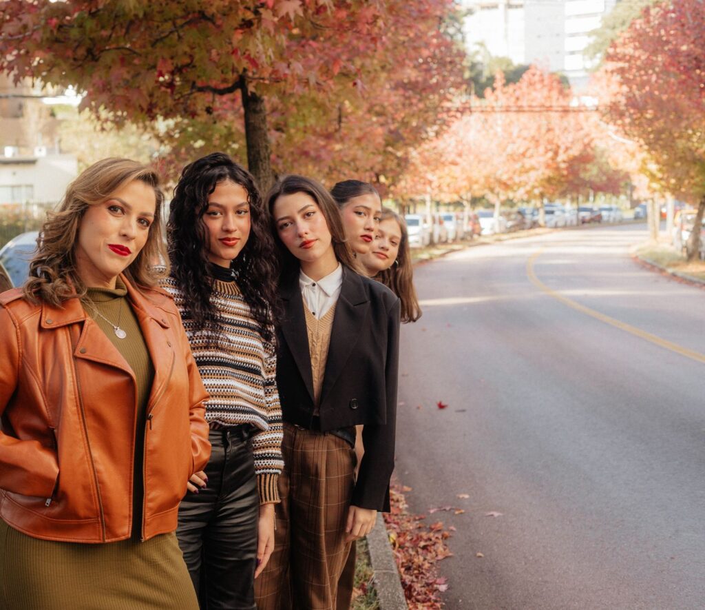 Group of stylish women posing on a tree-lined city street in autumn.