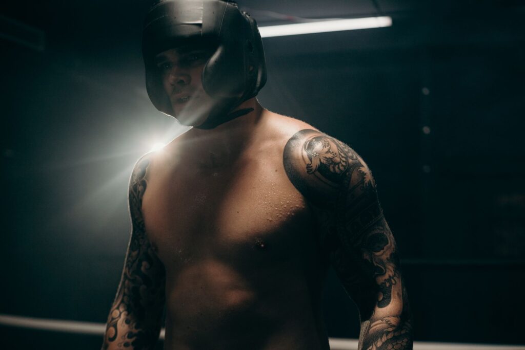 Focused boxer with tattoos training in dimly lit gym, wearing head guard.