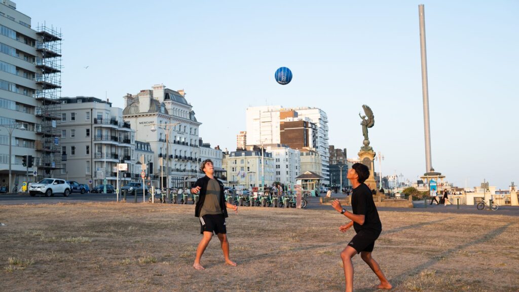 Two teenagers play football on a sunny summer day by Brighton's iconic seaside promenade.