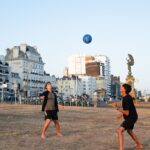 Two teenagers play football on a sunny summer day by Brighton's iconic seaside promenade.