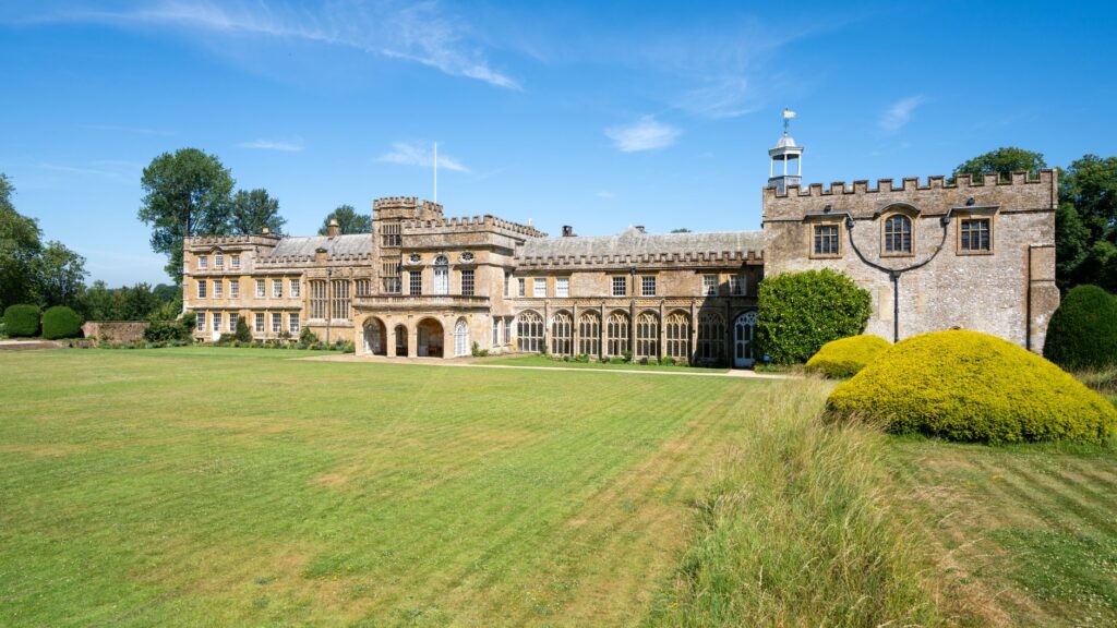 A serene view of Forde Abbey amidst lush greenery on a sunny day.