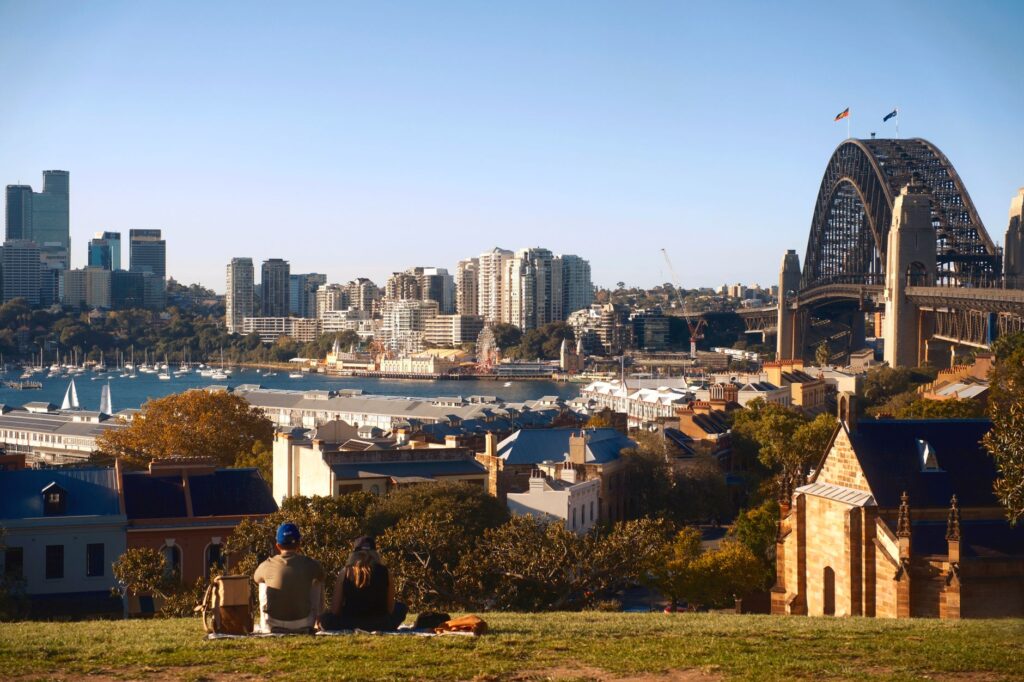 Couple sitting on a hill overlooking Sydney Harbour and the iconic Sydney Harbour Bridge.