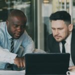 Two businessmen concentrating on a tablet, collaborating in a modern office setting.