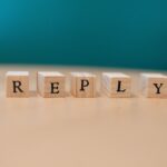 Close-up of wooden blocks spelling 'REPLY' on a table with teal background.