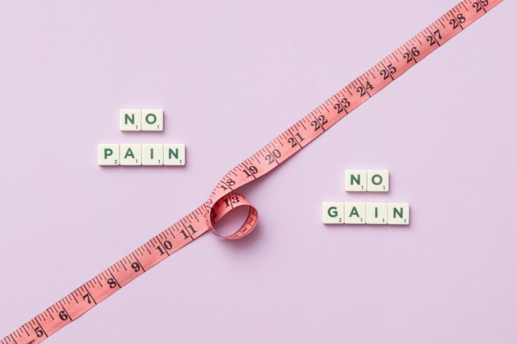 Pink tape measure with 'No Pain No Gain' spelled in Scrabble tiles on pink background.