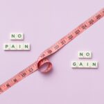 Pink tape measure with 'No Pain No Gain' spelled in Scrabble tiles on pink background.