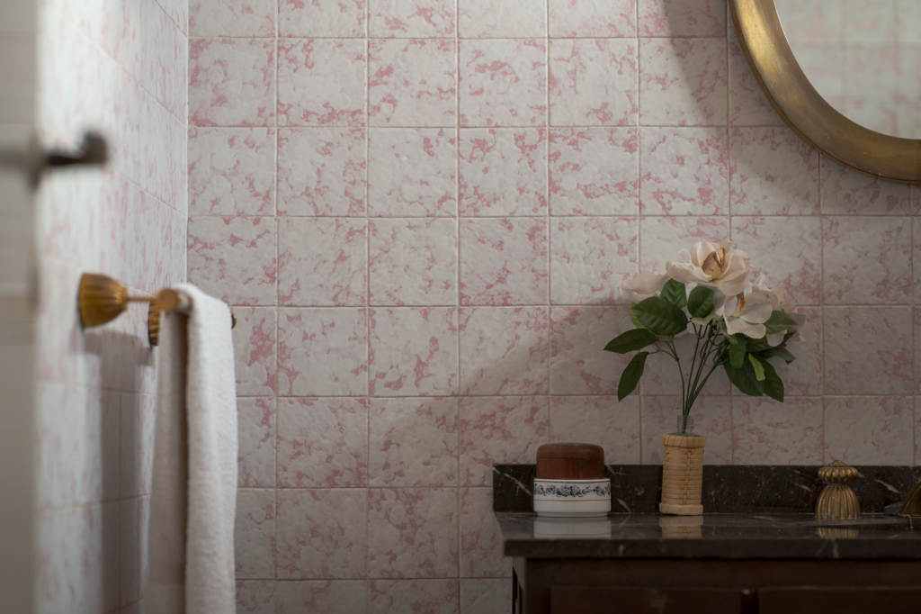 Charming bathroom scene with vintage tiles, a round mirror, and floral decoration.