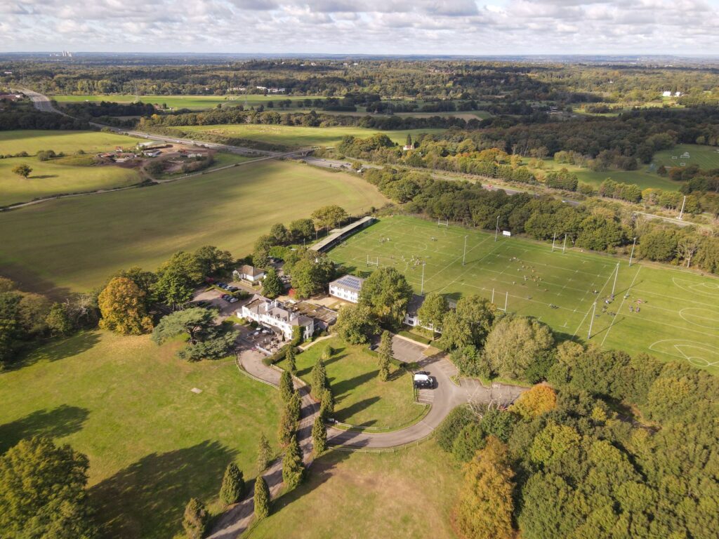 Spectacular aerial view of aged classic styled palace located in green grassy field surrounded by lush trees on sunny day in countryside