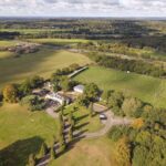 Spectacular aerial view of aged classic styled palace located in green grassy field surrounded by lush trees on sunny day in countryside