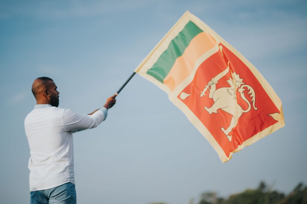 A man proudly waving the Sri Lankan flag outdoors under a clear sky.