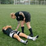 A female soccer player helps an injured teammate on a green soccer field during a game.