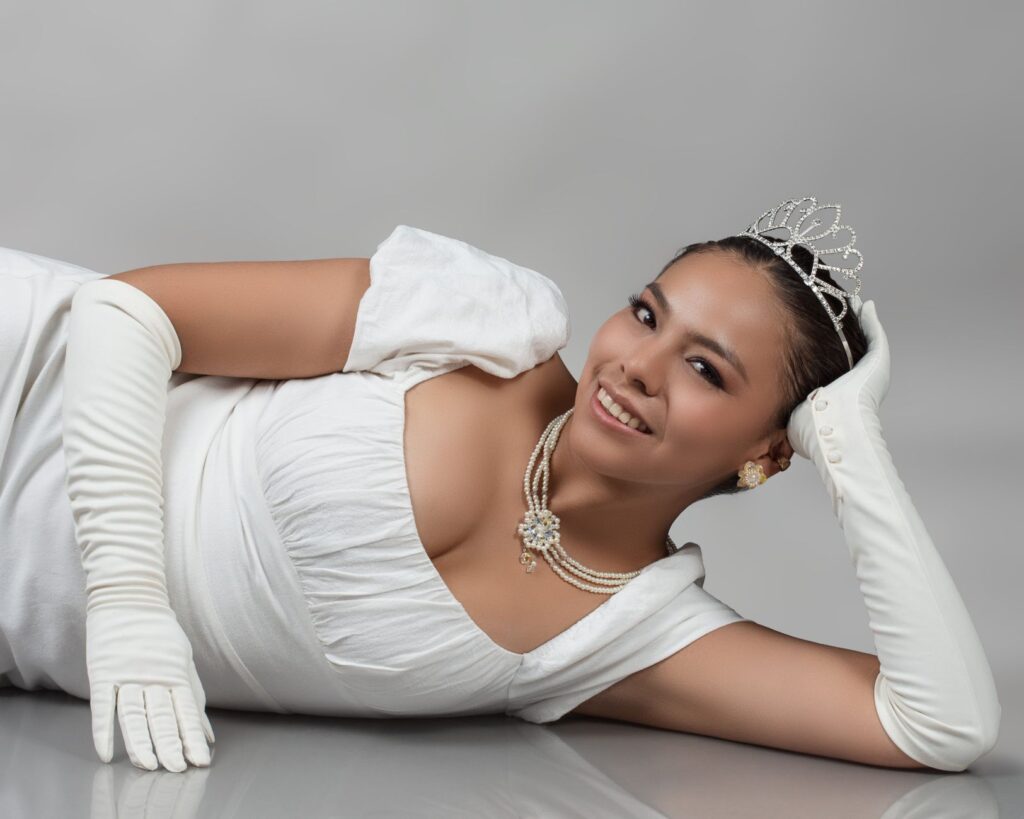 Portrait of a smiling woman in a white gown and tiara, exuding elegance and grace.