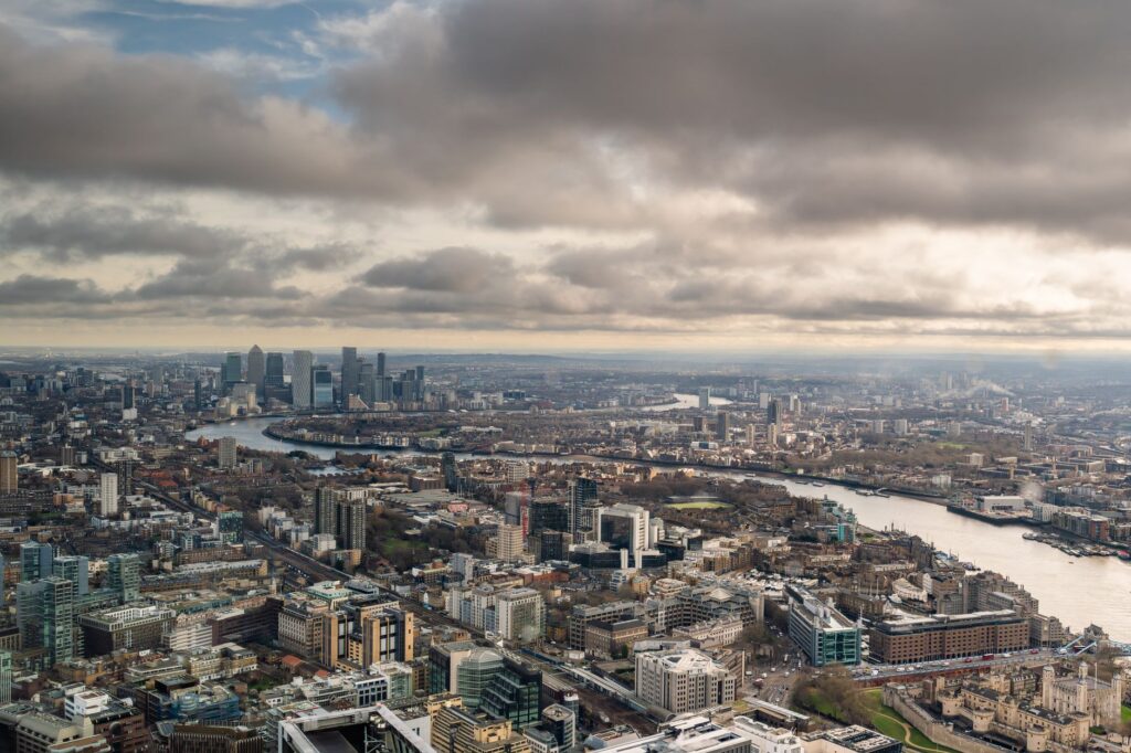 Stunning aerial shot of London's skyline with the iconic River Thames and Canary Wharf in view, under a dramatic sky.