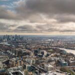 Stunning aerial shot of London's skyline with the iconic River Thames and Canary Wharf in view, under a dramatic sky.