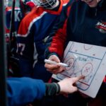 Hockey coach discussing tactics on a board with players during match break.
