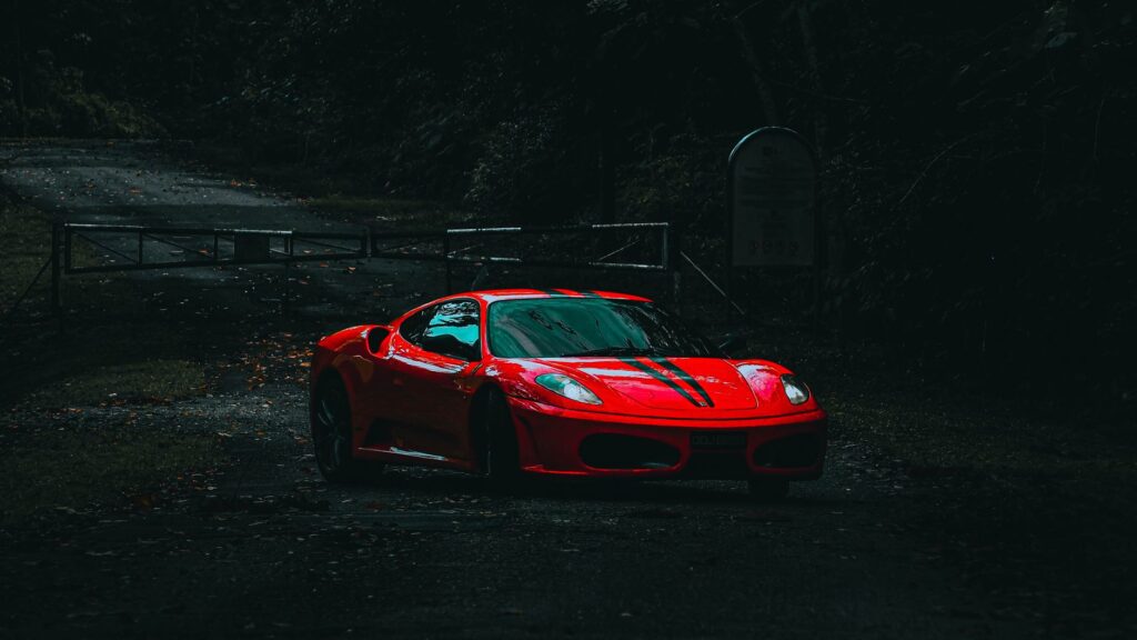Dramatic shot of a red sports car on a secluded, dark forest road.