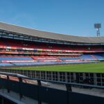Panoramic view of De Kuip stadium in Rotterdam with empty stands and a clear blue sky.