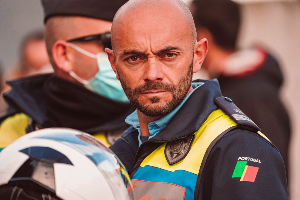 A focused Portuguese police officer in uniform holding a helmet outdoors.