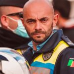 A focused Portuguese police officer in uniform holding a helmet outdoors.