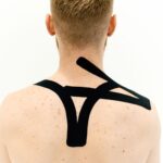 Black kinesio tape applied to man's back for therapeutic treatment on a white background.