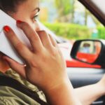 Close-up of a woman driving a car while talking on a smartphone, highlighting road safety concerns.
