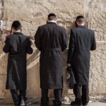 Back view of unrecognizable orthodox Jewish men in traditional religious clothes praying against Western Wall in Old City of Jerusalem